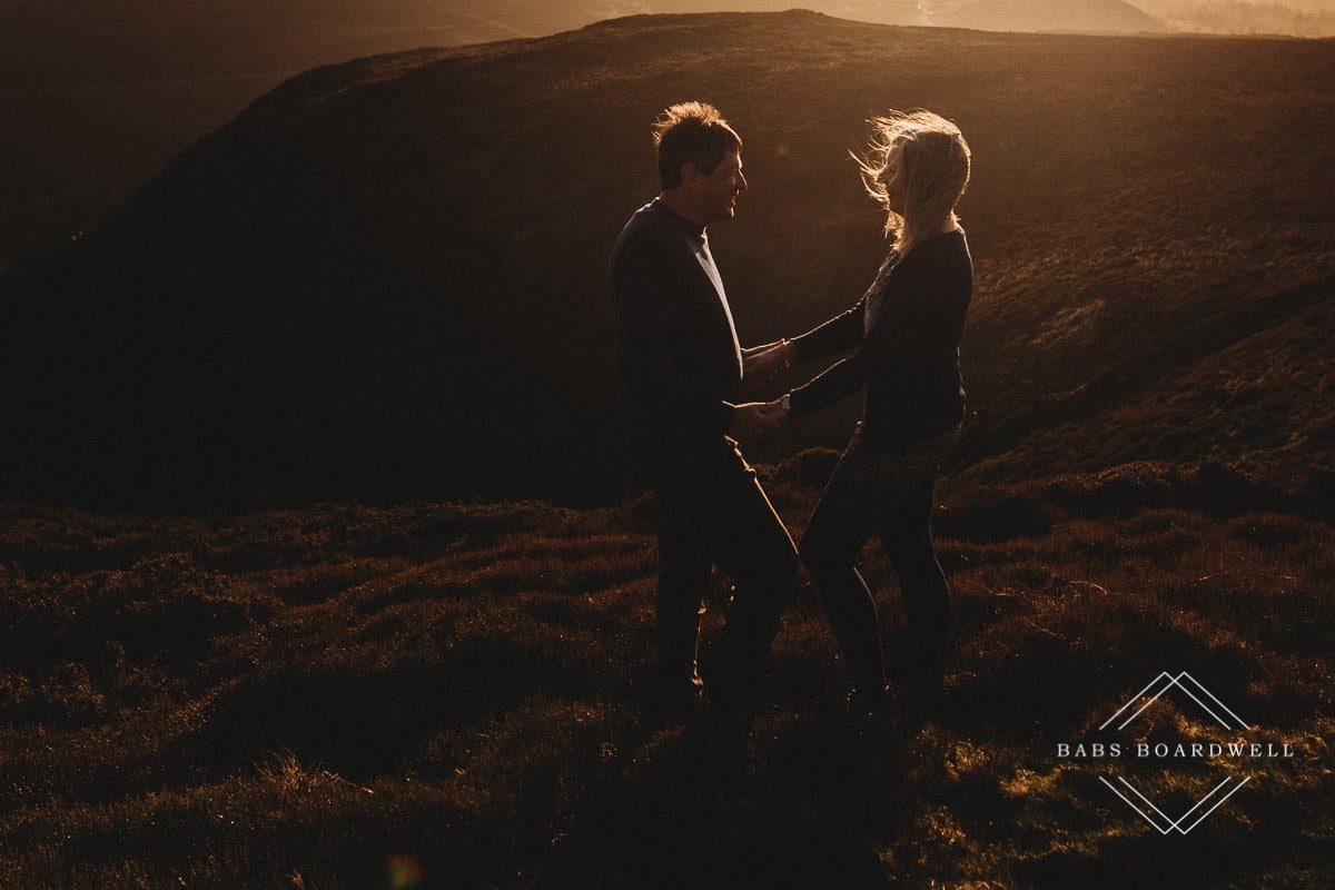 couple holding hands standing opposite one another and looking at each other at sunset