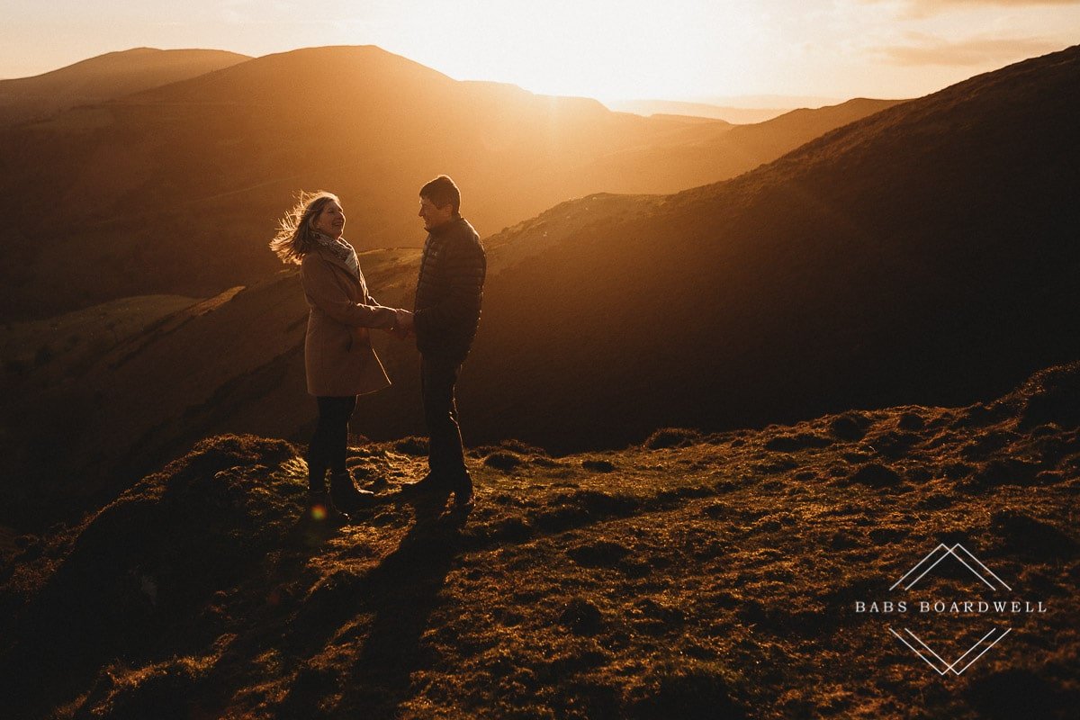 couple holding hands at sunset with the woman's hair blowing in the wind