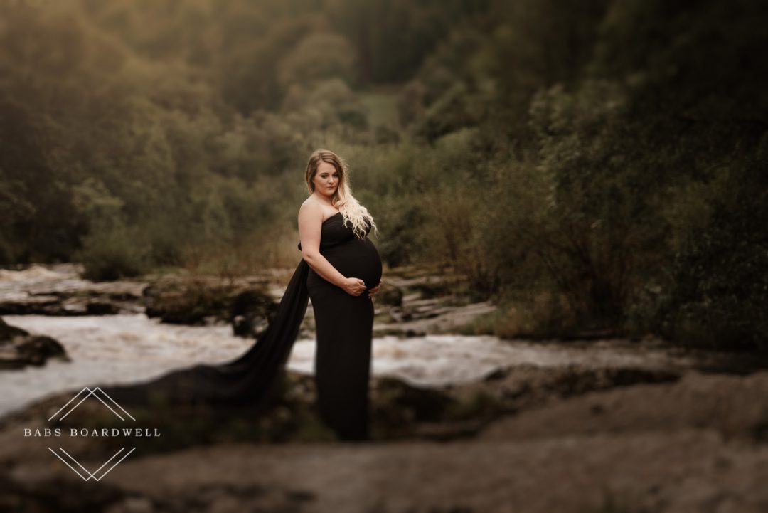 pregnant woman in black off the shoulder dress on a river bank