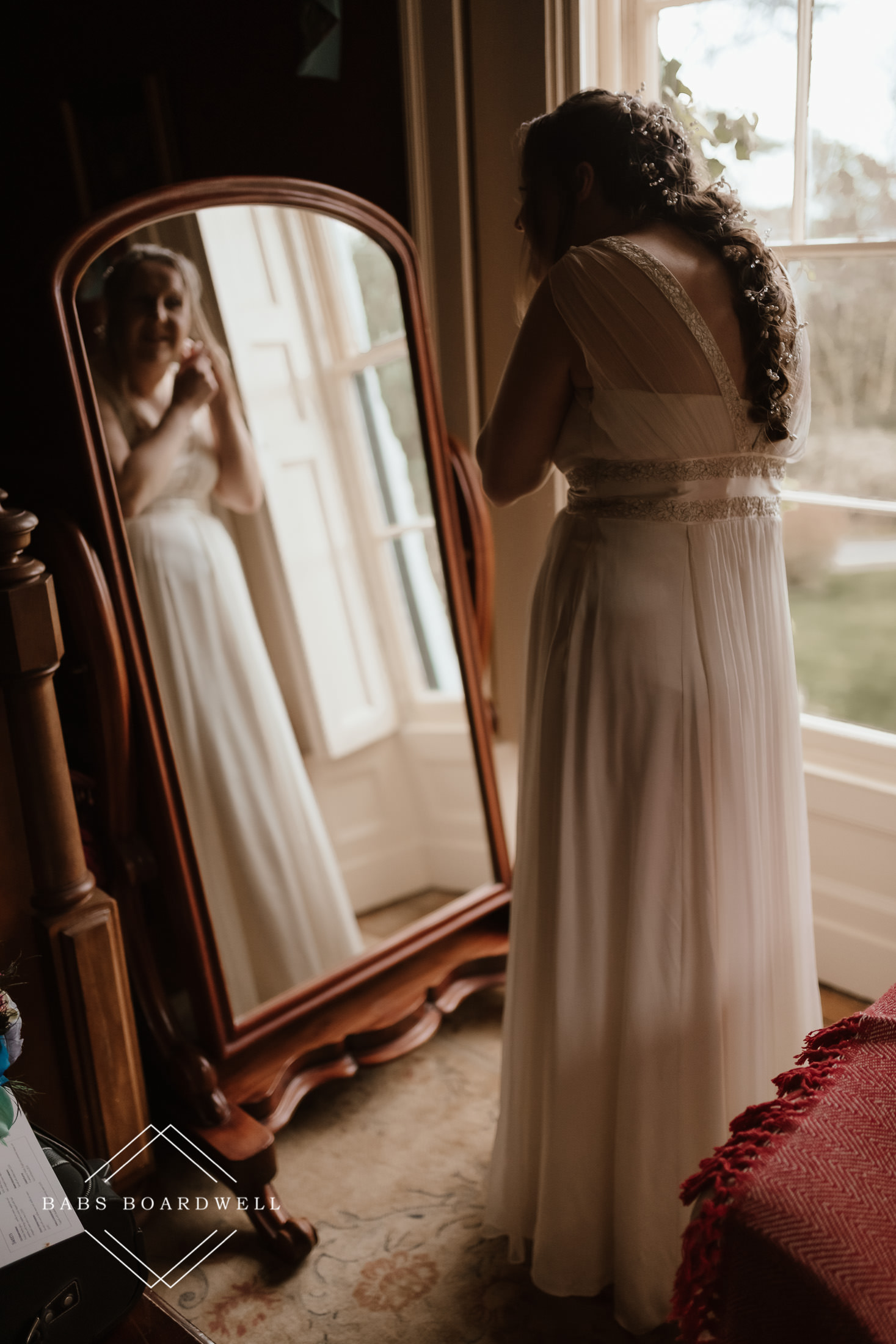 bride looking at herself in a mirror next to a window during bridal prep at a spring wedding at Plas Hafod