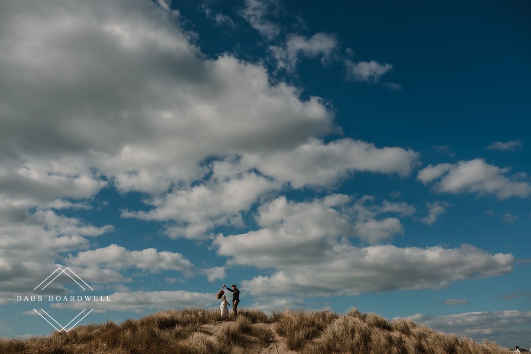 bride and groom on a sand dune at Barmouth Beach twirling on their elopement day by Snowdonia Wedding Photographer