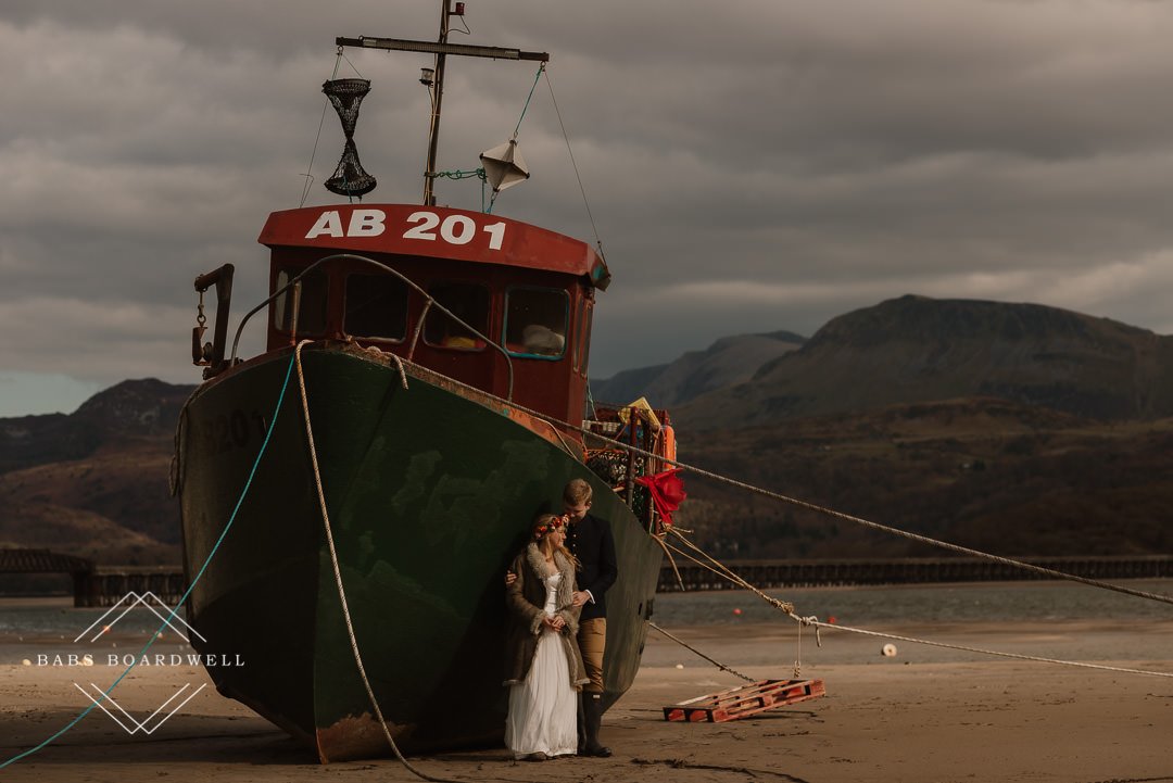 bride and groom standing by a boat in Barmouth Harbour