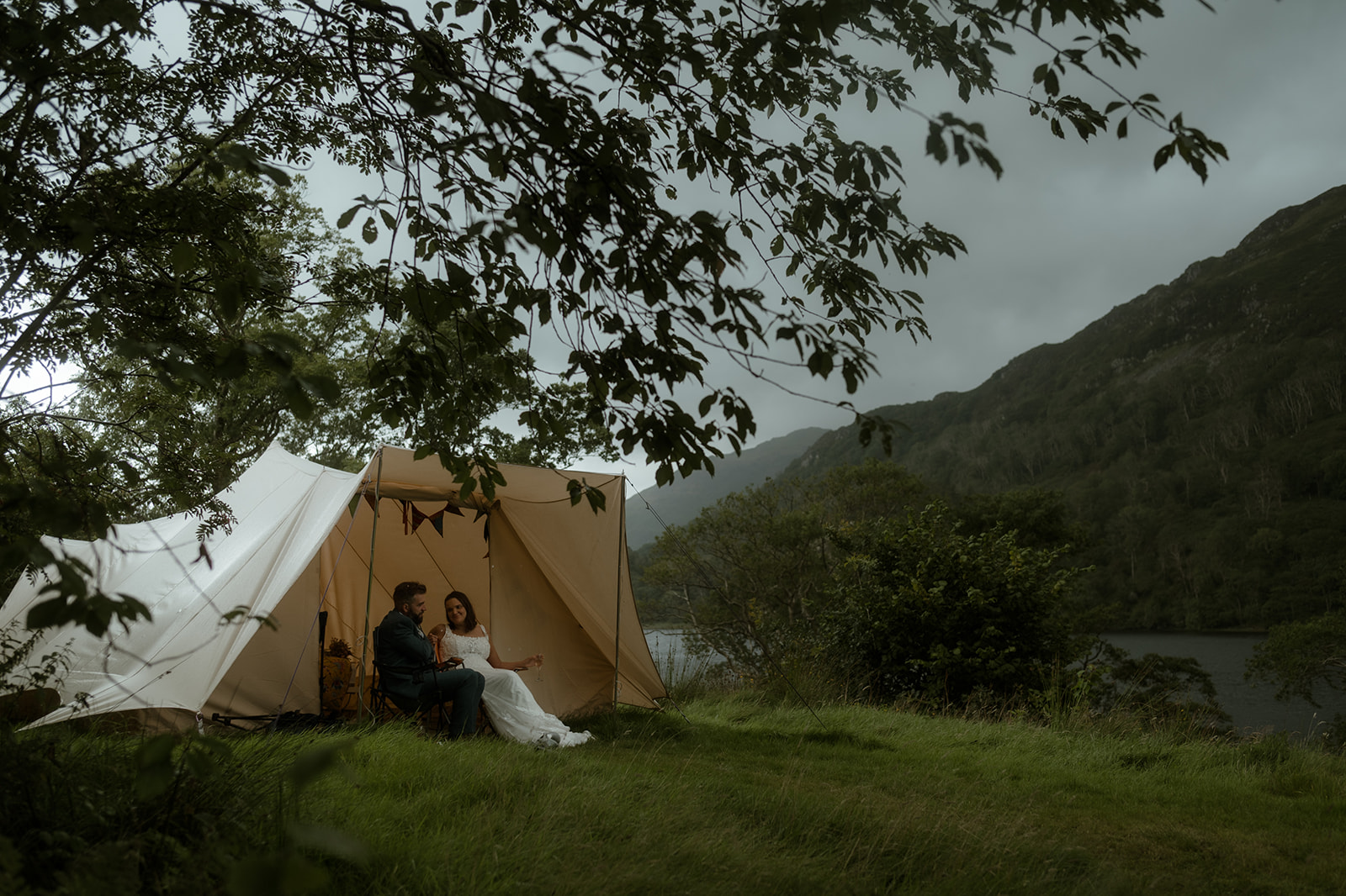 bride and groom sitting outside a bell tent in the rain overlooking mountains at Llyn Gwynant