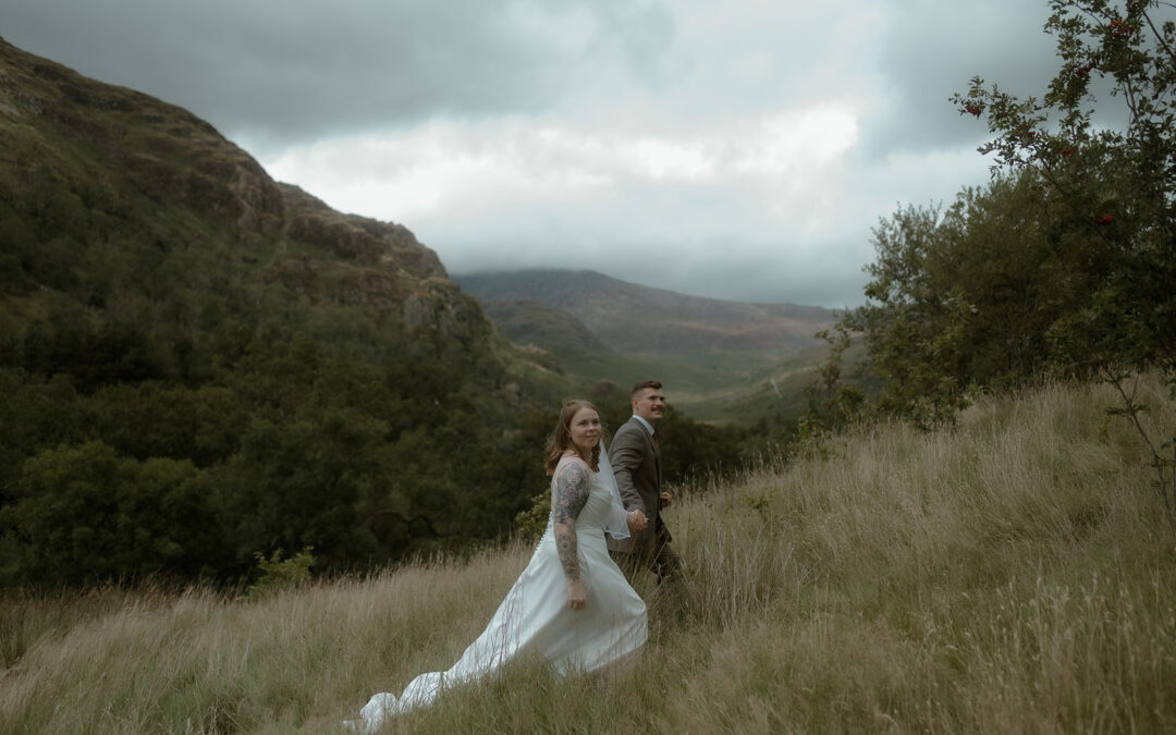 bride and groom holding hands walking uphill against the backdrop of a mountain around Llyn Gwynant on their small wedding day