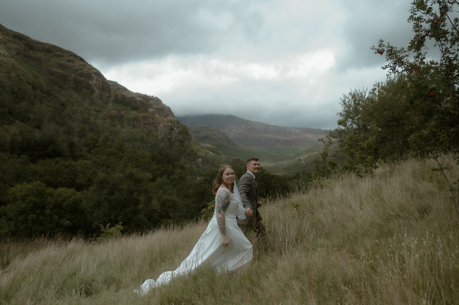 bride and groom holding hands walking uphill against the backdrop of a mountain around Llyn Gwynant on their small wedding day